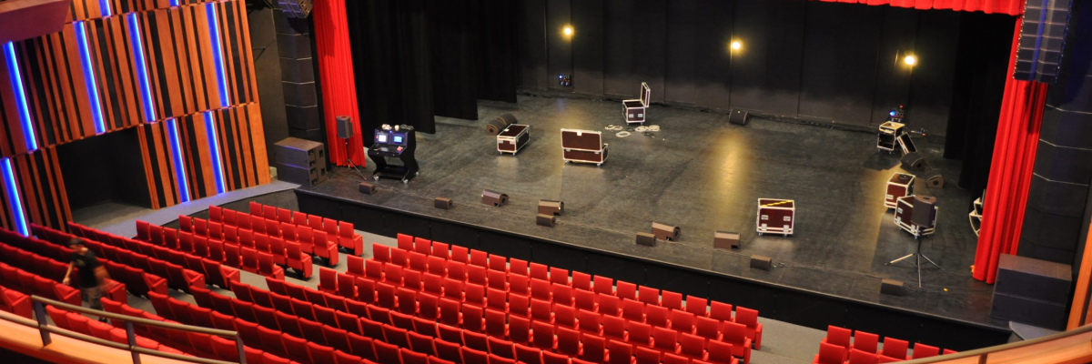 Salle de spectacle avec sièges, scène, rideaux, lumières et équipements audio.