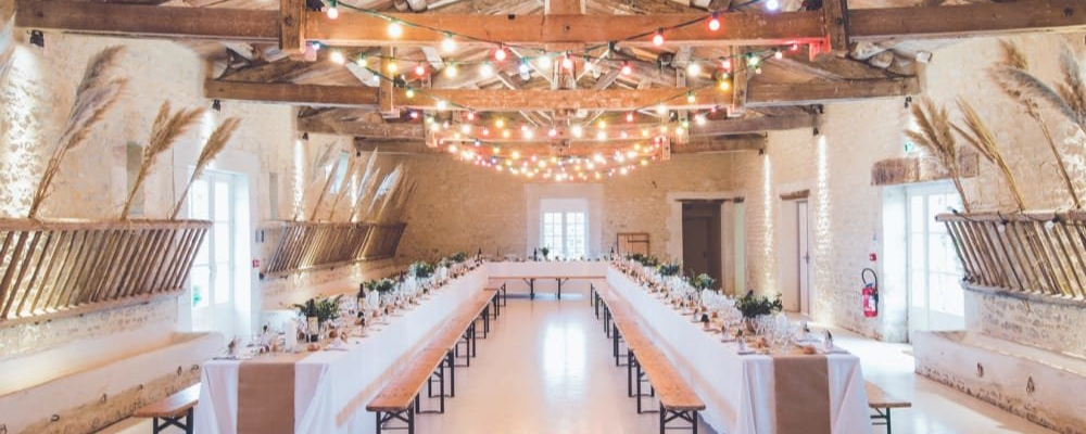 Salle avec tables, chaises, guirlandes lumineuses, et décorations florales.