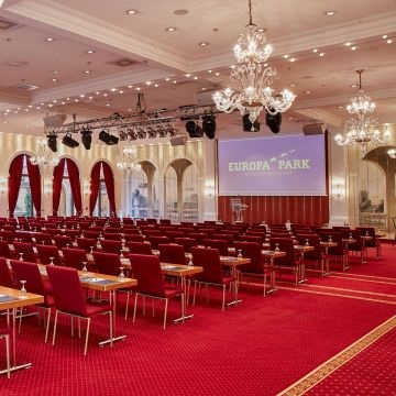 Salle avec chaises, tables, éclairages, écran, lustres et rideaux.