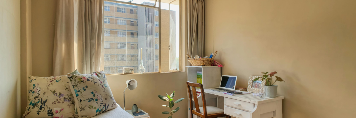 Chambre avec lit, bureau, chaise, ordinateur, plante et fenêtre.