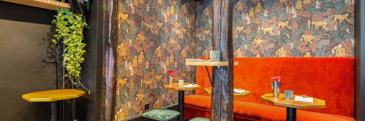 Bar avec tables, tabourets, étagère à bouteilles, plantes et cheminée.