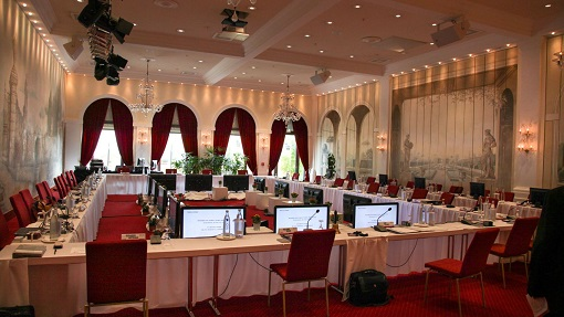 Salle de réunion avec tables, chaises, ordinateurs, écrans, projecteurs et rideaux.