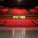 Salle de spectacle avec sièges rouges, scène et rangées de gradins.